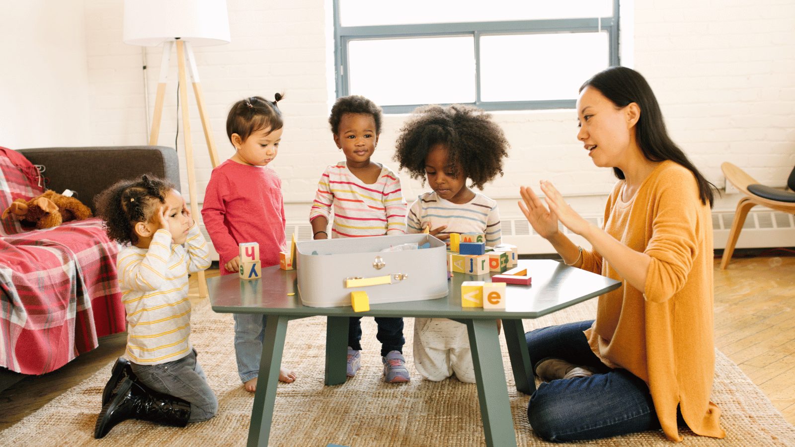A teacher sitting at a table with four other toddlers in a classroom setting